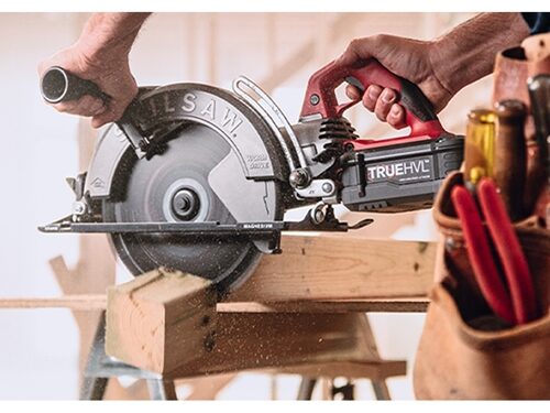  The 10-1/4 in. TrueHVL Cordless Worm Drive Saw cutting through a plank of wood with construction worker utilizing auxiliary handle and left-facing blade.