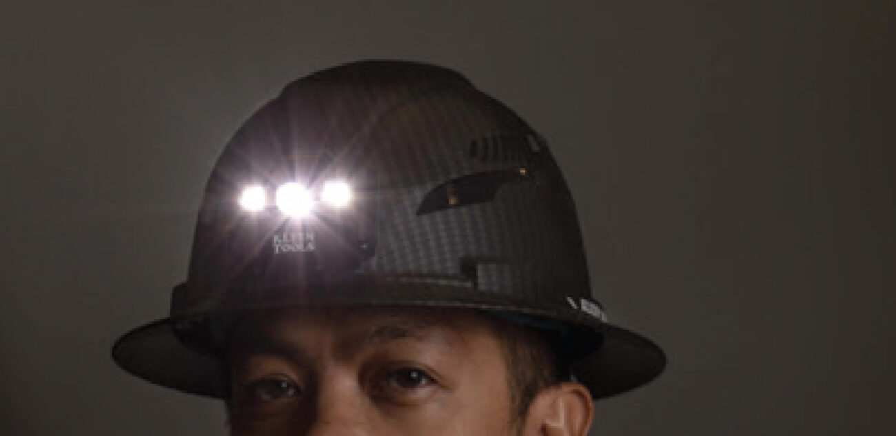 Construction worker wearing Klein KARBN hard hat in dark room with head lamp turned on